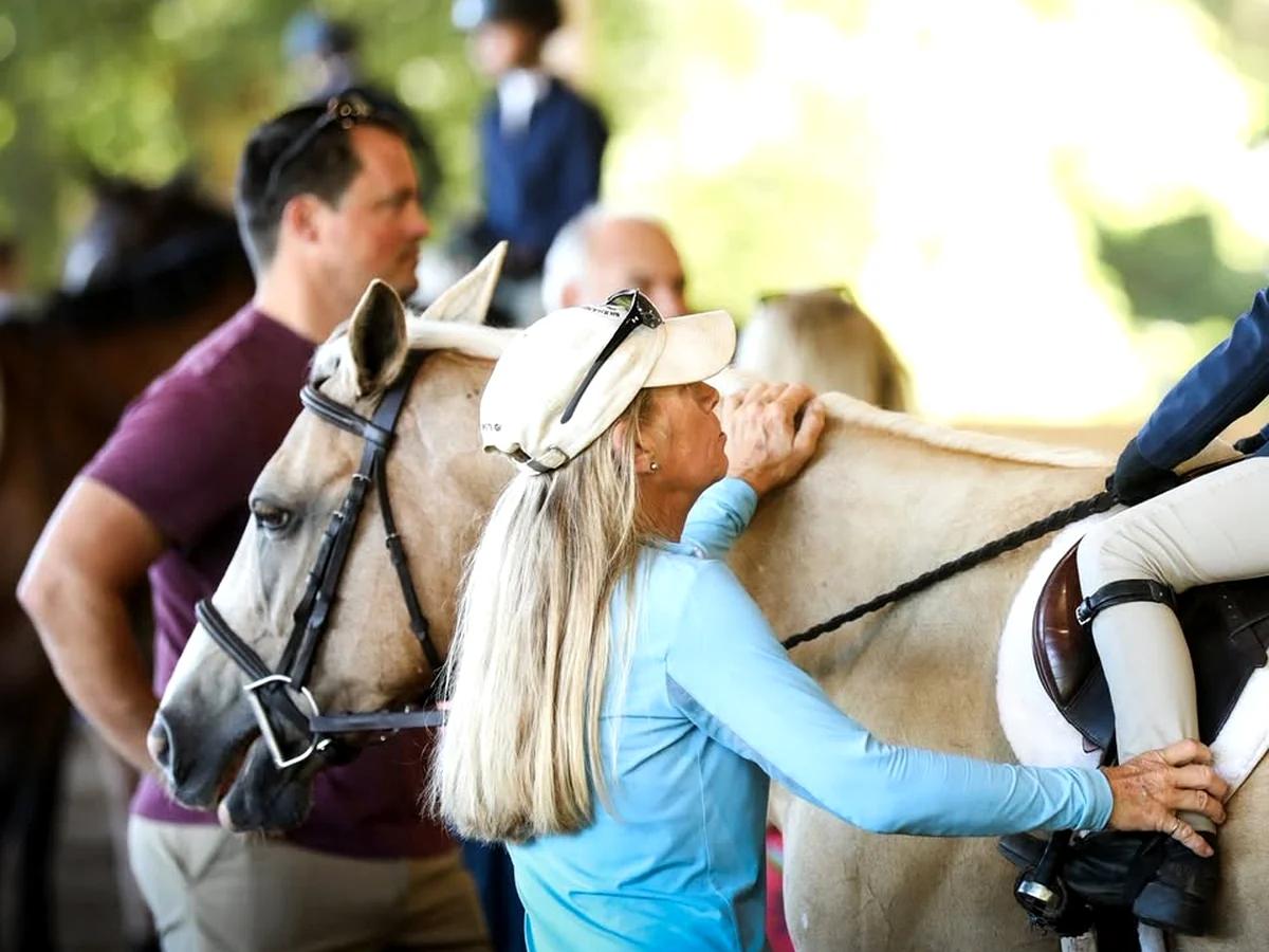 Close view of a light-colored pony with people nearby in a shaded barn setting.